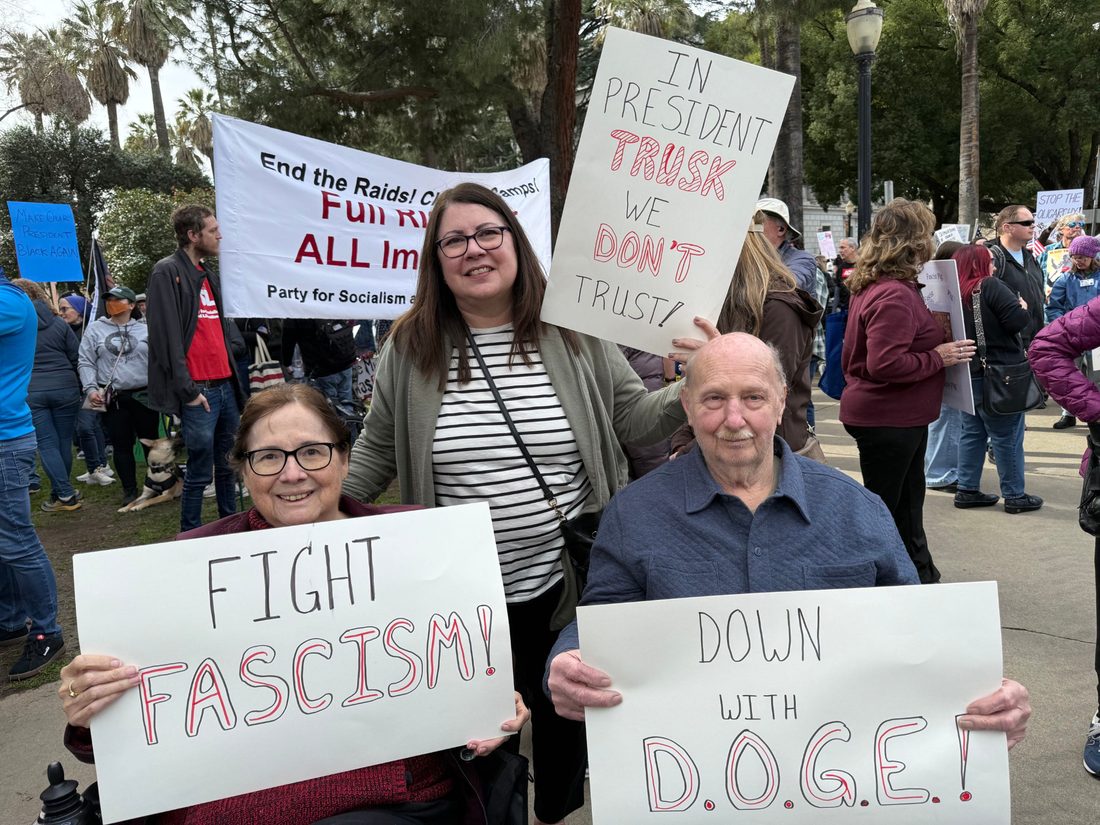 Demonstrators holding signs at an outdoor civic gathering