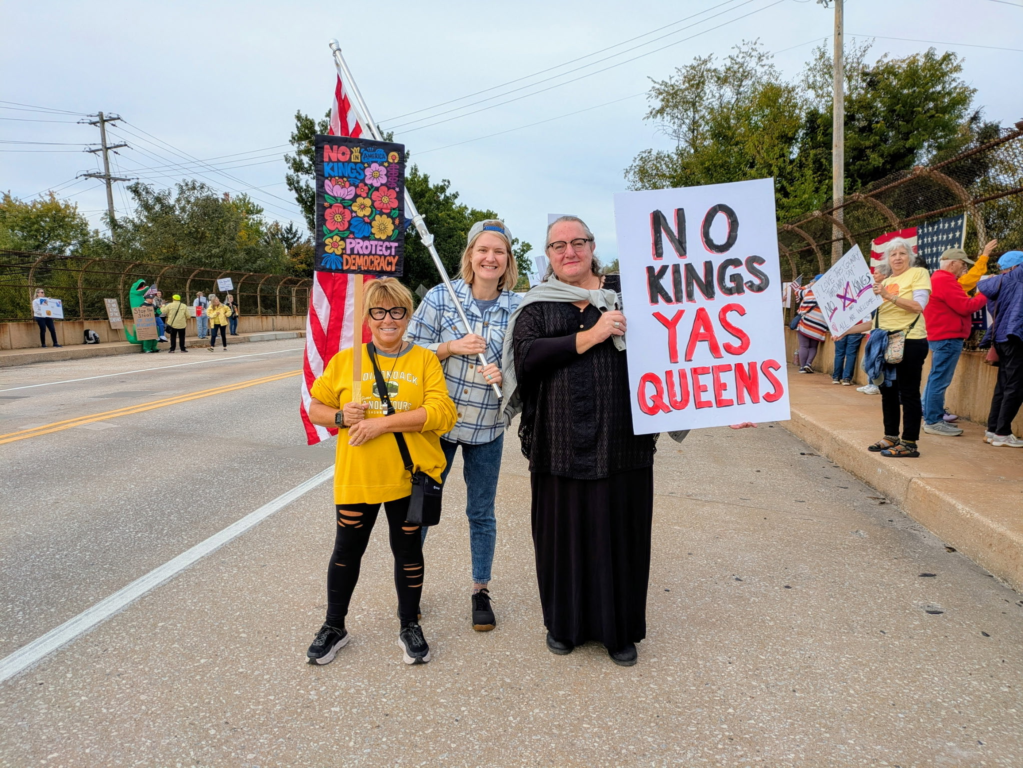 Protesters holding signs reading No Kings, Protect Democracy, and No Kings Yes Queens.